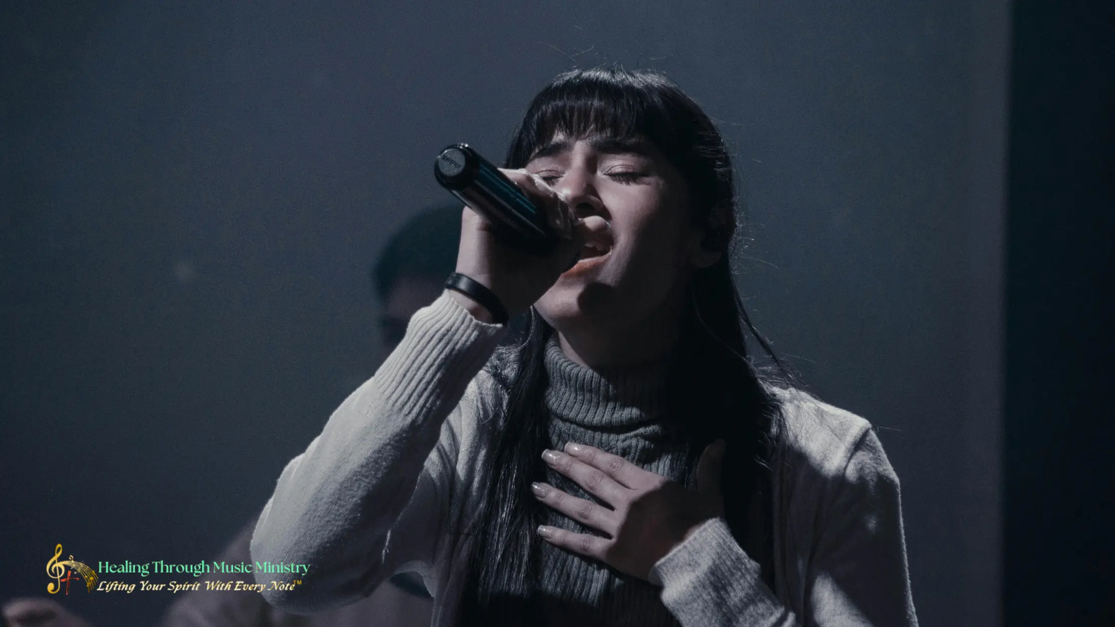 A woman singing passionately into a microphone on a dimly lit stage.